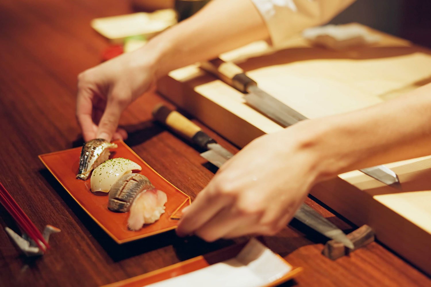 Chef plating omakase sushi on a red tray
